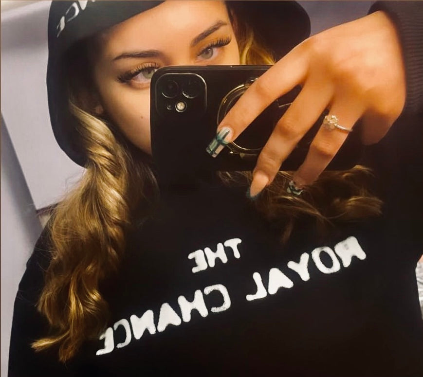 Person wearing a black hoodie with text "The Royal Chance", holding a phone.
